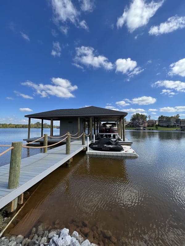 Covered dock with a boat lift, pontoon, and jet ski lifts under a bright blue sky