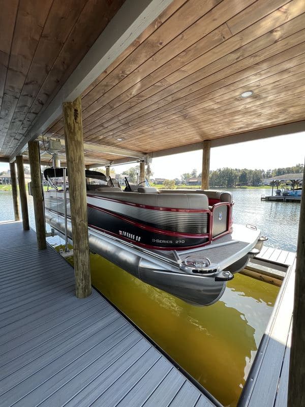Pontoon boat on its lift inside the covered slip, under a tongue-and-groove wood ceiling