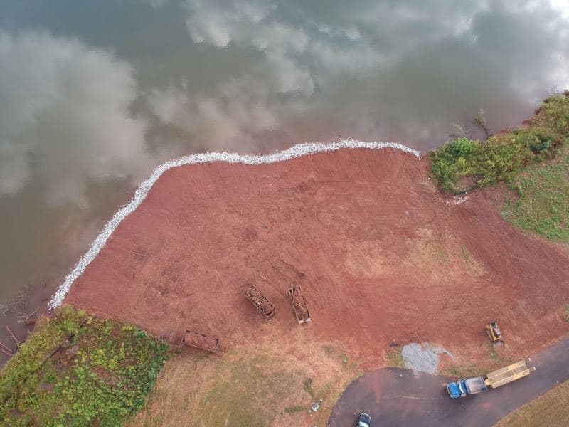 Overhead aerial of new rip rap stone lining the lake shoreline, with equipment staged on the graded lot