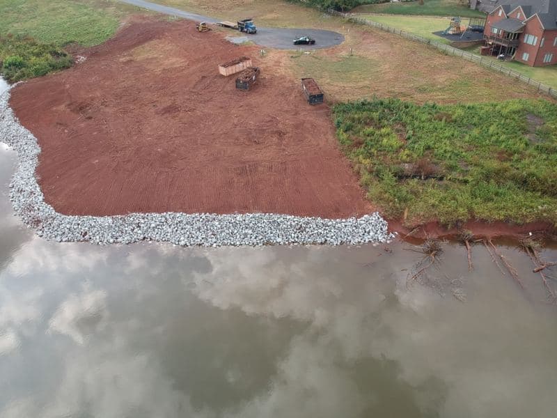 Aerial view of a straight run of rip rap shoreline stabilization along the lake edge, lakefront homes beyond