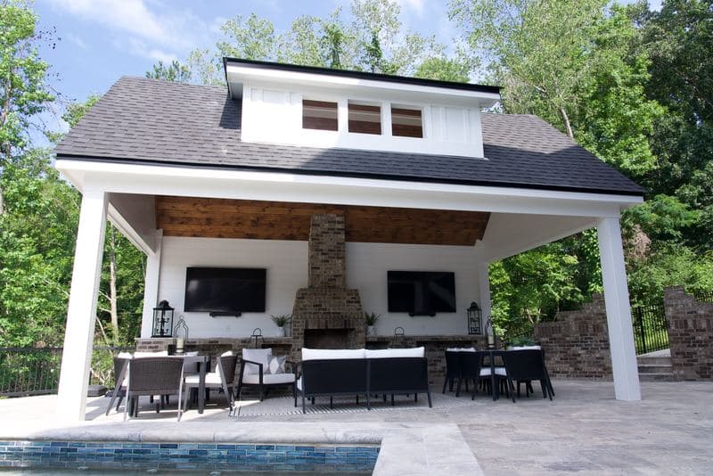 Poolside pavilion with white columns, stone fireplace, and outdoor living furniture