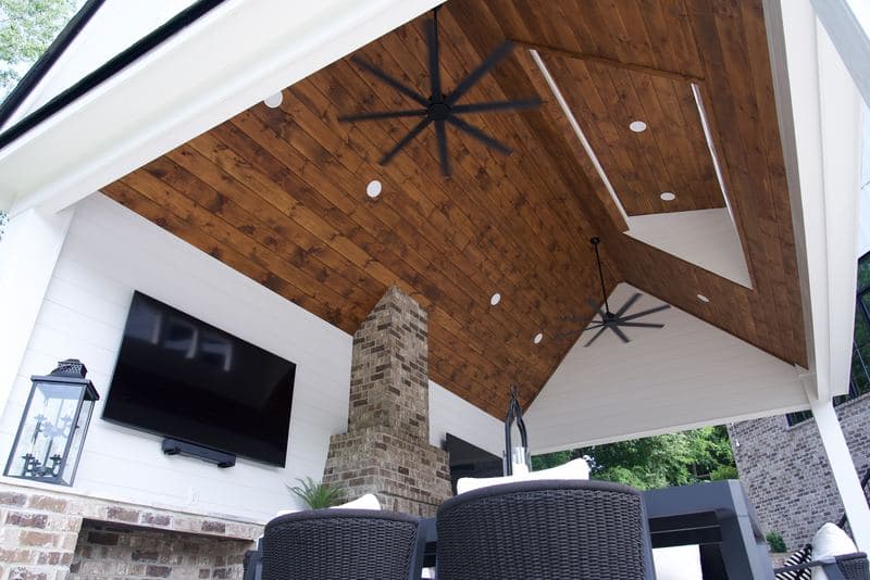Vaulted wood-plank ceiling with fans over the pavilion, stone fireplace and TV below