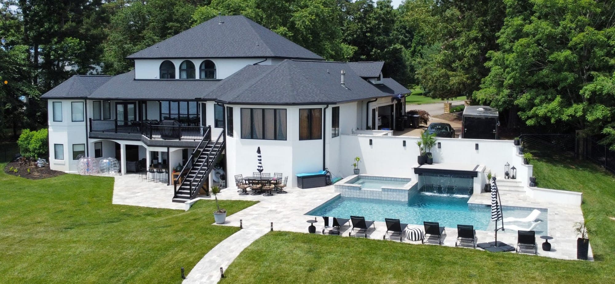 Aerial view of a pool and spa with a stone patio behind a white home in Lenoir City, TN