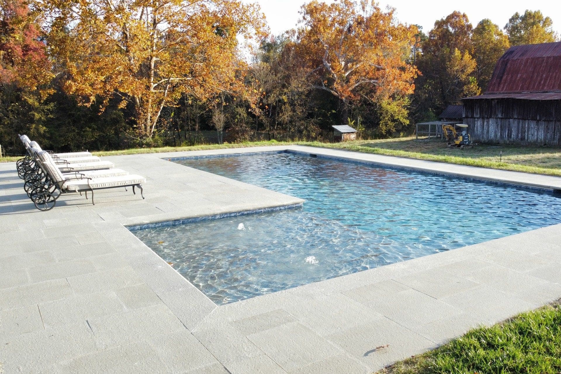 Rectangular pool with a stone deck and lounge chairs, autumn trees beyond, in Knoxville, TN