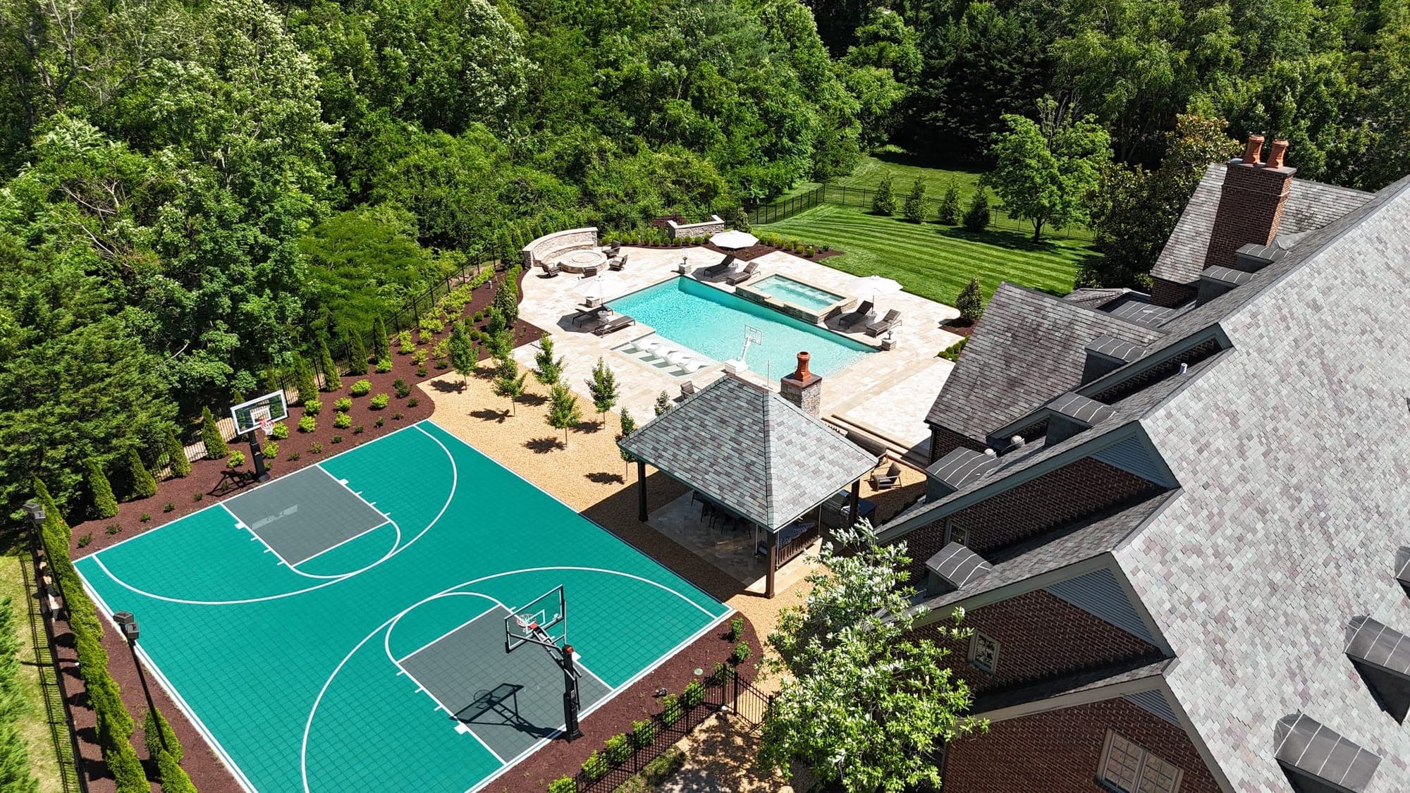 Aerial view of a Knoxville, TN backyard with a pool and spa, stone-roofed pavilion, patio and teal basketball sport court