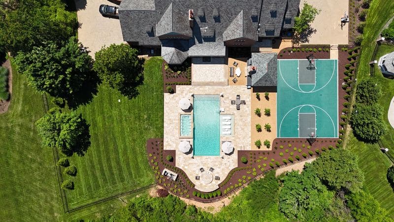 Straight-down aerial of the whole backyard: house, pool and spa, patio, pavilion, sport court, and curved fire-pit terrace