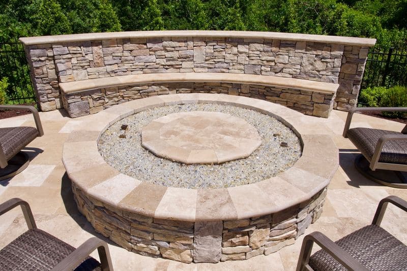 Round stone fire pit with a gravel surround and a curved built-in stone bench wall