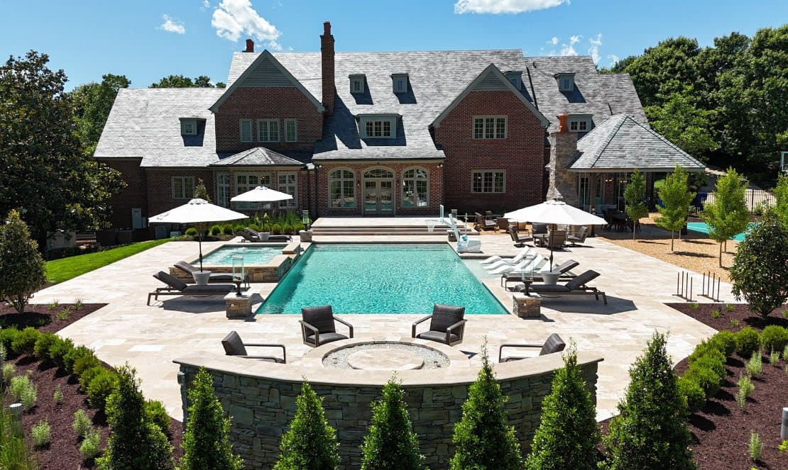 After: pool, spa, travertine patio, and stone fire-pit wall behind the same house