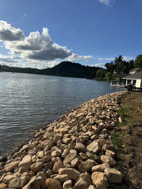 Finished river rock shoreline stabilization curving along the lake under a dramatic cloudy sky