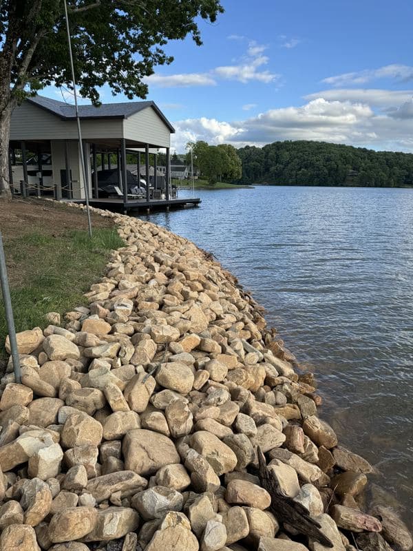 River rock shoreline stabilization leading toward a covered boat dock on the lake