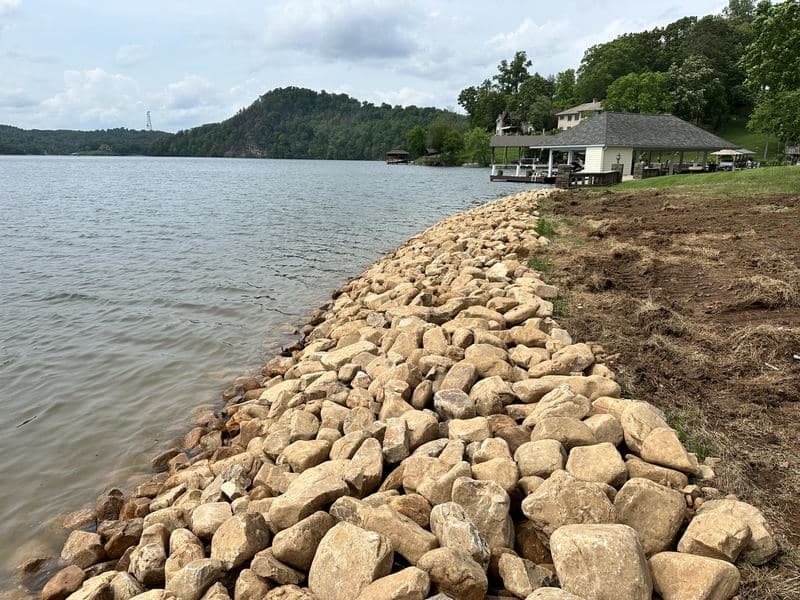 River rock shoreline stabilization along a lakefront property with a covered boat dock beyond