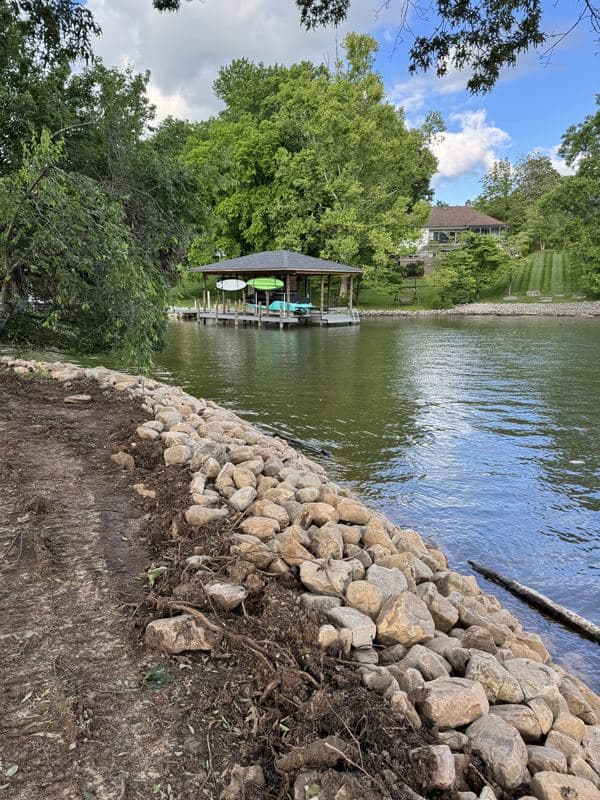 Finished river rock shoreline wrapping a quiet cove with a covered dock across the water