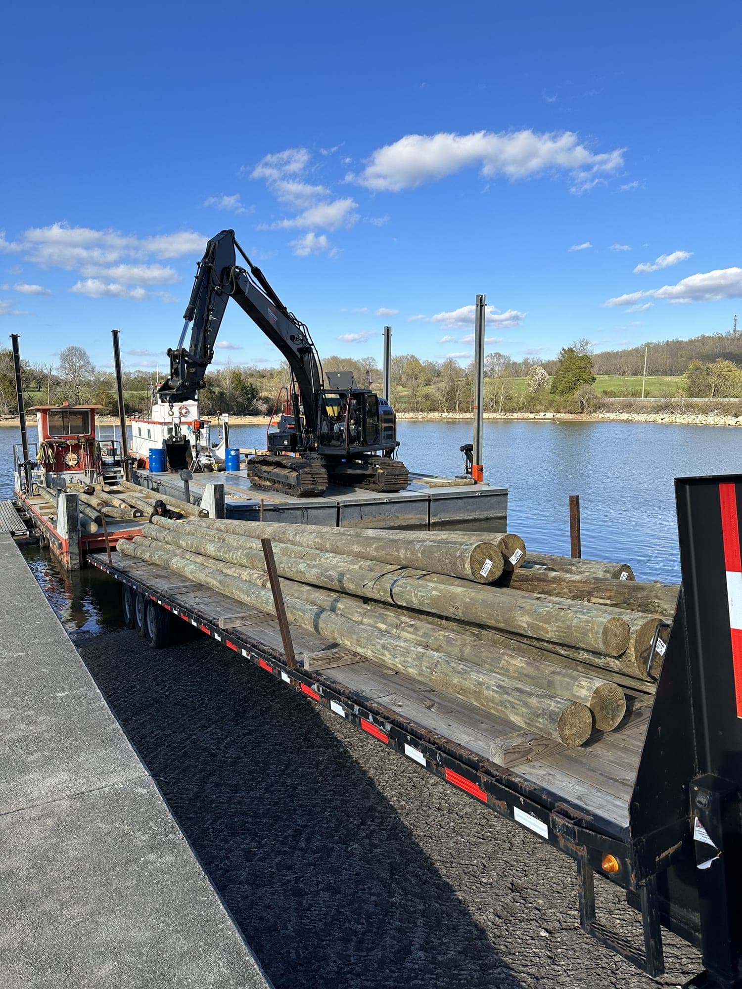 Company barge and excavator with treated pilings staged on a trailer at the lakeshore