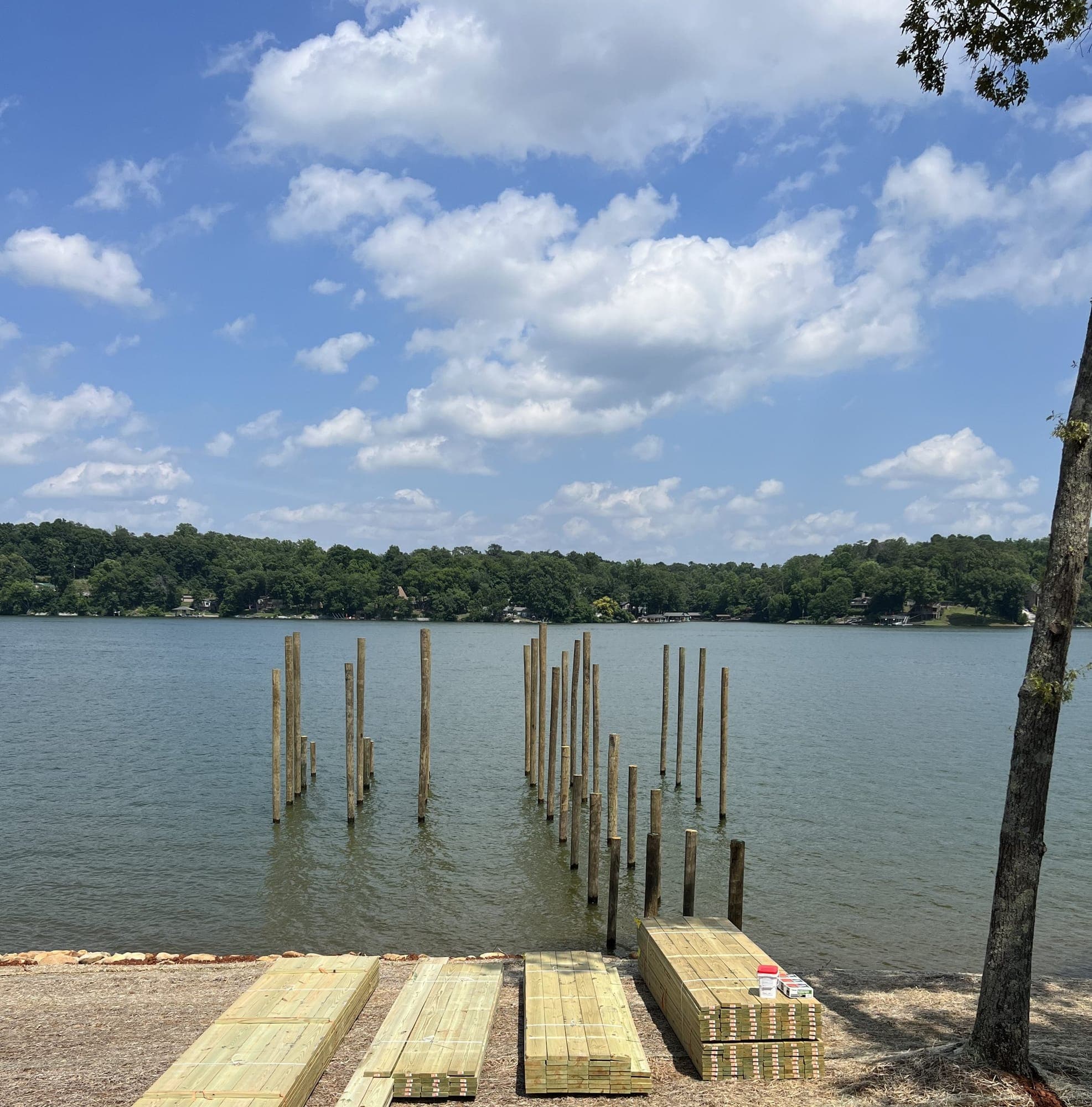 Marine pilings driven in the lake with lumber staged on shore for dock construction
