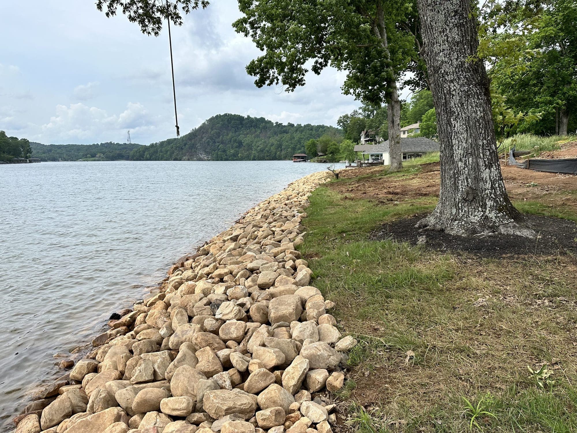 Fresh river rock shoreline stabilization along a grassy lakefront lawn with a shade tree on an East Tennessee lake